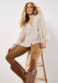 En beige blus med volanger och knäppning, kombinerad med bruna mockaleggings och bruna broderade cowboystövlar.