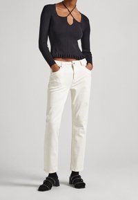 Svart ribbat långärmad topp med en nyckelhålöppning och volangkant, kombinerad med vita raka jeans och svarta klacksandaler med nitar.