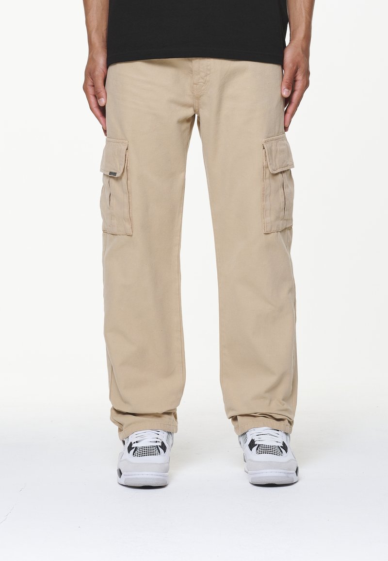 Beiga cargobyxor med flera sidofickor, tillverkade av slitstarkt tyg. Avslappnad passform och rak ben-design. Bärs med vita sneakers.