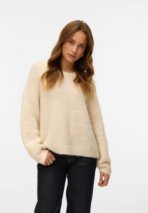 Cremefarbener Strickpullover mit strukturiertem Muster und lässiger Passform, ausgestattet mit langen Ärmeln und Rundhalsausschnitt, kombiniert mit dunklen Jeans.