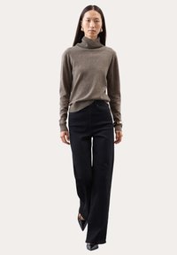 Grauer Rollkragenpullover mit geripptem Ausschnitt, kombiniert mit schwarzen weit geschnittenen Hosen. Das Model trägt schlichte schwarze Spitzenheels.