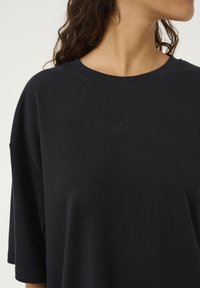 Sort bomulds T-shirt med rund halsudskæring og korte ærmer. Har et broderet logo på brystet og en løs, afslappet pasform.