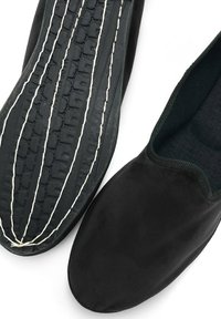 Zapatos negros tipo slip-on con un upper liso, suela de goma con dibujo texturizado y costuras decorativas, interior de forro de tela suave.