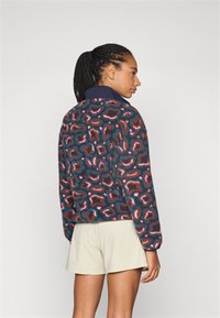 Bunte Fleecejacke mit einem dunkelblauen Grundton und einem buntgemusterten abstrakten Tierdruck. Lange Ärmel mit einem hohen Kragen.