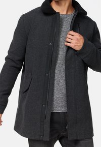 Grå uldfrakke med en sort falsk pelskrave, lynlås foran og to sidelommer. Glat tekstur med en afslappet pasform.