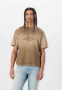 Brun gradient kortærmet t-shirt med frontgrafik og afslappet pasform samt blødt bomuldsstof, parret med lysvaskede slidte jeans.