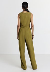 Jumpsuit verde oliva realizzato in tessuto testurizzato; design senza maniche con schiena alta, cintura in vita e pantaloni a gamba larga.