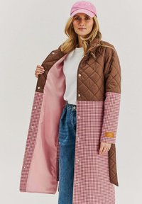 Prošívaný hnědý kabát s růžovým vzorem houndstooth, kontrastní podšívkou, zacvakávacími knoflíky a nášivkou s logem na rukávu.