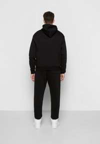 Sort hættetrøje med kængurulomme og justerbar hætte, kombineret med matchende bukser, alt i blødt, børstet stof; hvide sneakers.