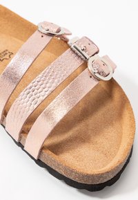 Růžově zlaté syntetické sandály se třemi texturovanými popruhy, nastavitelné stříbrné přezky a konturovanou béžovou stélkou na černé podrážce.