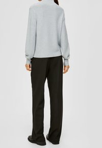 Helles graues Sweatshirt mit hohem Kragen und gerippten Manschetten, kombiniert mit dunklen, weiten Hosen. Glatte Textur, minimales Design, keine sichtbaren Muster.