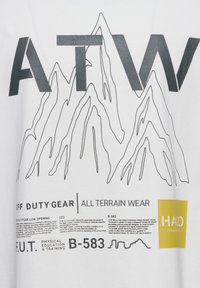 Hvid t-shirt med en bjergkontur grafik i sort, hvor "ATW" er tydeligt vist, og tekst der beskriver udendørsbeklædningens specifikationer.