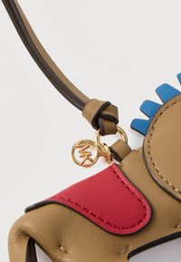 Κοντινό πλάνο από ένα μπρελόκ από καφετί δέρμα σε σχήμα σκύλου με κόκκινο αυτί, μπλε περιλαίμιο και χρυσό διακριτικό λογότυπο MK σε λουράκι με θηλιά.