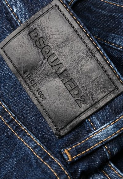 Tissu en denim bleu foncé avec des coutures orange contrastantes ; présente une étiquette en cuir noir texturé estampillée avec "DSQUARED2" et "SINCE 1964."