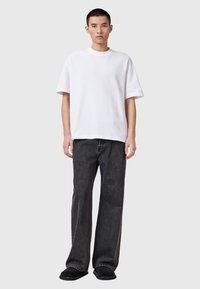 Camiseta de algodón blanca de manga corta, combinada con jeans de mezclilla negros de corte relajado y un ligero desgaste, llevada con zapatos negros tipo slip-on.