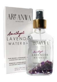 Bouteille en verre transparent contenant de l'eau de lavande avec des cristaux d'améthyste violets à l'intérieur, avec un bouchon-pompe doré et une boîte blanche affichant les détails du produit.
