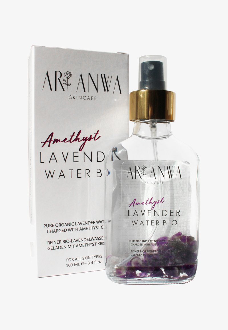 Bouteille en verre transparent contenant de l'eau de lavande avec des cristaux d'améthyste violets à l'intérieur, avec un bouchon-pompe doré et une boîte blanche affichant les détails du produit.