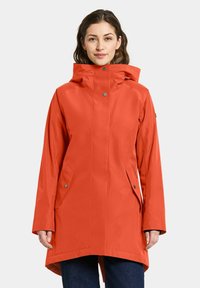 Veste imperméable rouge avec capuche, fermetures à boutons-pression sur le devant, poches latérales, et un ourlet arrière légèrement plus long. Texture lisse et coupe ajustée.