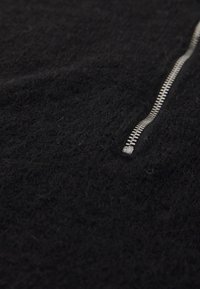 Close-up of a silver zipper on textured black fabric, partially zipped, highlighting fabric's soft and fuzzy surface.