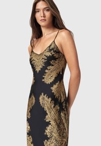 Sort kjole med gyldent paisley-mønster, tætsiddende pasform, spaghettistropper og en glat, blank stoftekstur. Elegant design og detaljer.
