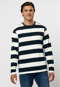Langarm gestreept shirt in marineblauw en crème, gemaakt van zachte stof. Heeft een ronde hals en een klein rood logo op de borst.