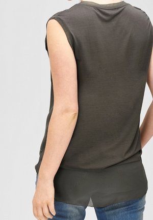 Oliven grøn ærmeløs top med glat tekstur, udskåret ryg og transparent nederste lag, parret med denim jeans.