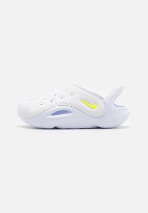 Hvid slip-on sandal med ventilationshuller, en gul Nike-swoosh og åben hælstrop på en ensfarvet baggrund.