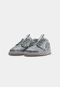 Sneaker grigie con un design testurizzato, caratterizzate da una combinazione di materiali lucidi e opachi, chiusura con lacci e suola in gomma.