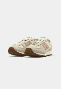Beige Sportchuhe mit einer strukturierten Oberseite, hellrosa Akzenten, einer weißen Zwischensohle und einer braunen Gummisohle mit einem Zickzackmuster.