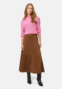 Maglione rosa lavorato a maglia con maniche corte a sbuffo abbinato a una gonna a pieghe in camoscio marrone. La modella indossa stivali neri al ginocchio.