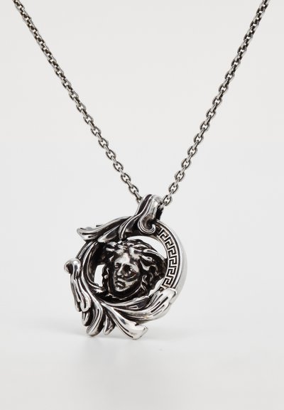 Silver pendant necklace featuring a detailed face surrounded by swirling leaves and a geometric border, suspended on a chain link.