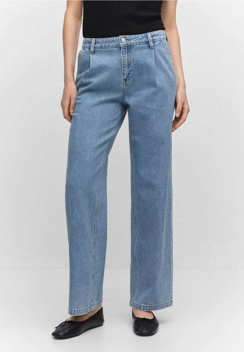 Femme portant un jean droit taille haute bleu clair, associé à des ballerines noires et un haut noir sans manches.