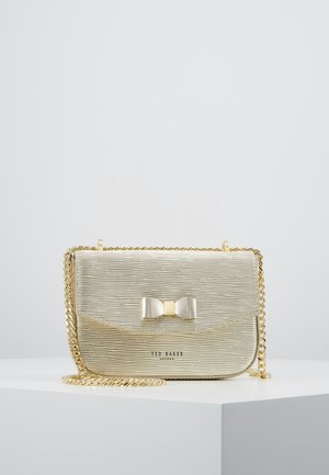 Petit sac bandoulière doré texturé avec bandoulière chaîne et détail nœud sur le rabat, présenté sur une surface blanche.