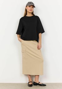 Sort oversized t-shirt, beige midi nederdel med lommer og sorte blanklæder sko. En leopardmønstret cap fuldender outfittet.