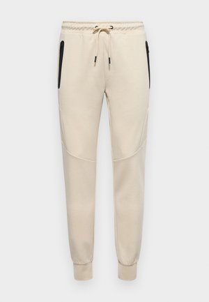 Lichtbeige sweatpants met een drawstring tailleband, zijritsen en taps toelopende manchetten met textuuraccenten op de zijpanelen.