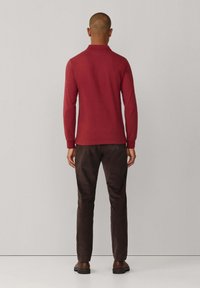 Polo à manches longues de couleur bordeaux avec col, associé à un pantalon marron foncé. Coupe simple et texture lisse, adapté pour une tenue décontractée.