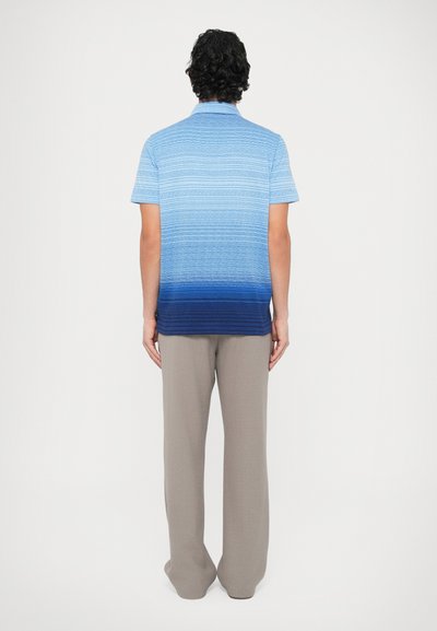 Polokošeľa s krátkym rukávom v prechode farieb od svetlomodrej po tmavomodrú s vodorovnými pásmi. Kombinovaná so svetlosivými, voľnými nohavicami.