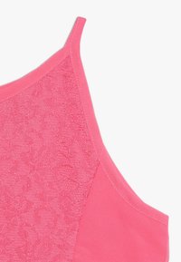 Roze mouwloos topje met dunne bandjes en een voorpaneel met een subtiel bloemenlacemotief op een effen stof achtergrond.