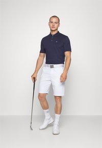 Navy polo shirt with logo, white shorts, white belt, white socks, and golf shoes; holding a golf club, simple design, smooth textures.