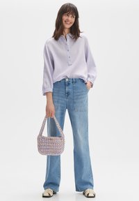 Camicetta button-up lilla, jeans a gamba larga blu chiaro e borsa in lavender intrecciata. Le scarpe sono crema con dettagli neri.