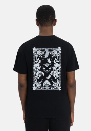Zwarte katoenen t-shirt met een witte grafische bloemen- en dierenprint op de achterkant, omlijst door een decoratieve rand. Korte mouwen.