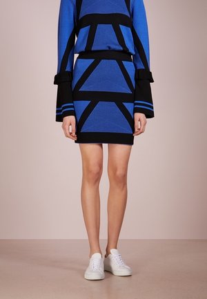 Niebiesko-czarna sukienka dzianinowa z geometrycznymi wzorami, długimi rękawami z falbanami, do tego białe tenisówki.