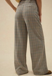 Pantalons à jambes larges dans un motif à carreaux marron, noir et blanc. Fabriqués en tissu léger avec une texture douce et de subtils poches arrière.