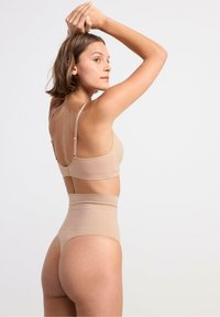 Set di lingerie beige composto da un bralette con spalline sottili e una culotte a vita alta, realizzato in un tessuto liscio e elasticizzato con cuciture minimali.
