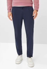 Chinos blu navy con una texture liscia, due tasche frontali e una vestibilità slim, abbinati a sneakers bianche.