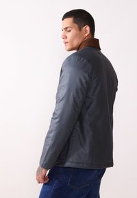 Men's dark gray jacket with a corduroy brown collar, smooth texture, classic fit, and side pockets. Worn over blue jeans.