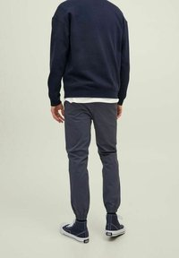 Uomo vestito con felpa blu navy, pantaloni jogger grigi scuri con polsini elasticizzati e sneakers alte blu navy, visto di spalle.