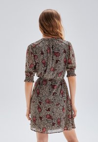 Vestido ajustado de manga corta en una tela de estampado animal beige adornada con patrones rojos de paisley, con una cintura fruncida y una silueta fluida.