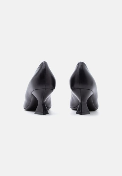 Ζευγάρι μαύρα γυναικεία παπούτσια μεσαίου τακουνιού από δέρμα, εμφανιζόμενα από πίσω σε λευκό φόντο.