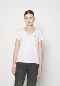 Fehér pamut póló V nyakkal és rövid ujjakkal. Az elülső bal mellrészen egy kicsi piros Levi's logó található. Egyszerű, klasszikus szabás.
